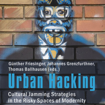 A graffiti of a man in white shirt, black suit, and Mexican wrestler mask is painted on an orange brick wall. Text says "Urban Hacking: Cultural Jamming Strategies in the Risky Spaces of Modernity."